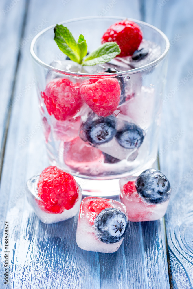 glass with frozen berries in cubes on wooden desk background