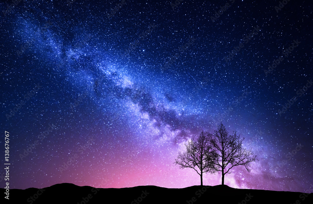 Starry sky with pink Milky Way. Night landscape with alone trees on the hill against colorful milky 