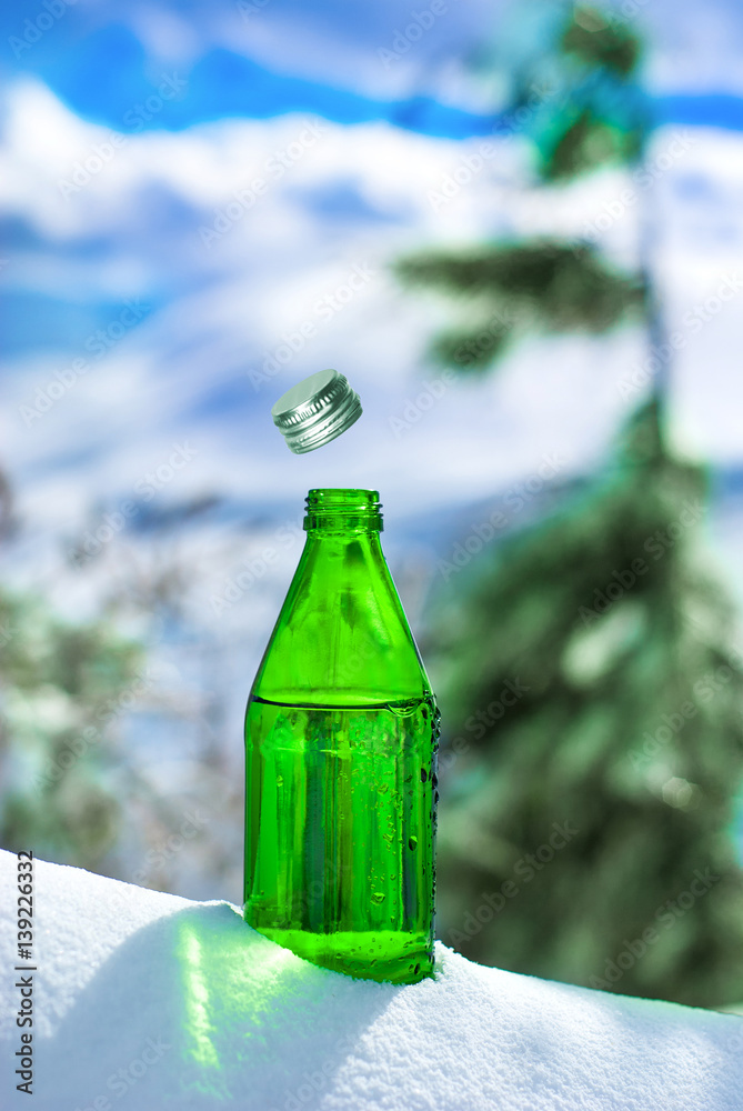 Open glass bottle of mineral water on the backdrop of Alpine scenery