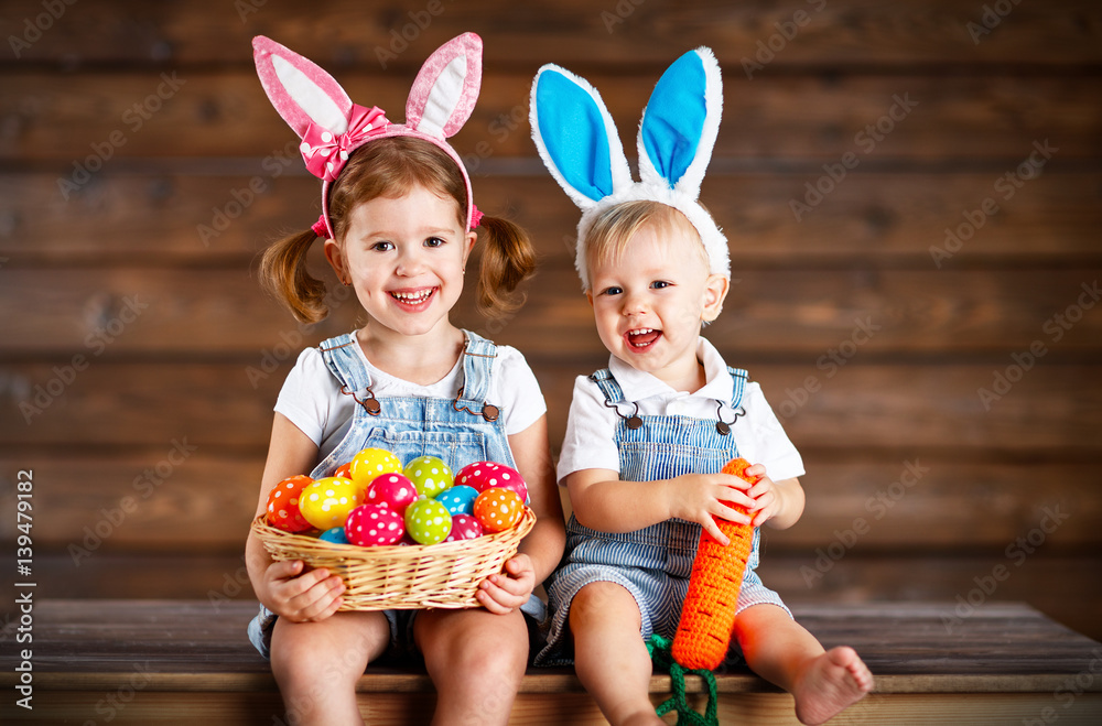 Happy kids boy and girl dressed as Easter bunnies with basket of eggs on  wooden .