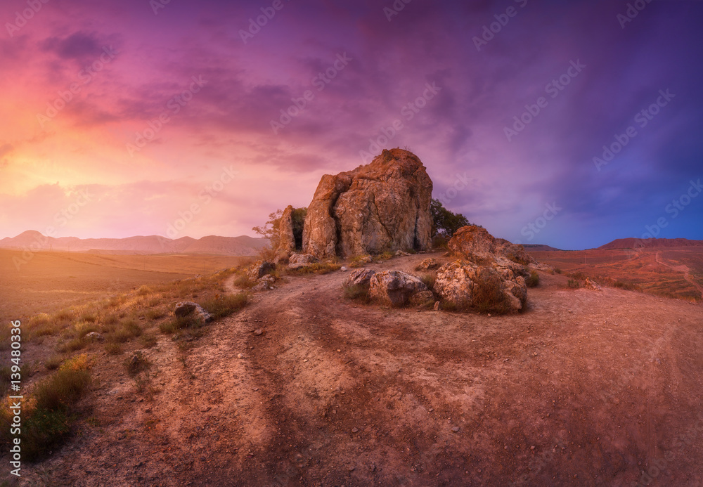 Desert with lonely rocks against multicolored cloudy sky at sunset. Blue, purple and red clouds. Pan