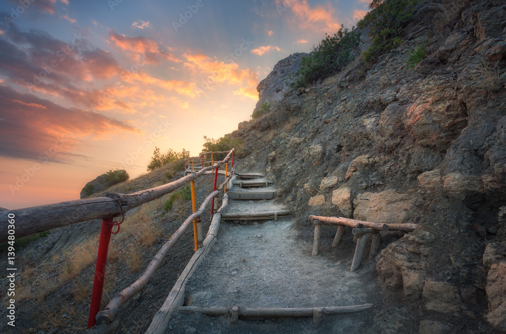 Stone stairs with wooden railing in the mountains at sunset. Landscape with mountain path and rocks 