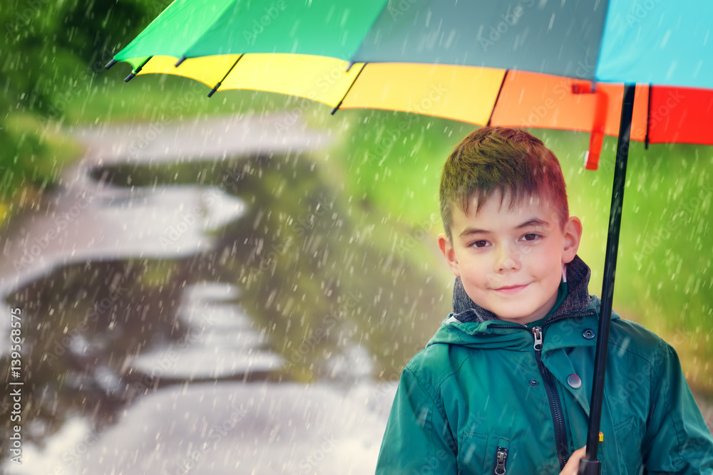 Child walking in puddle on rainy weather. Boy holding colourful umbrella under rain in summer
