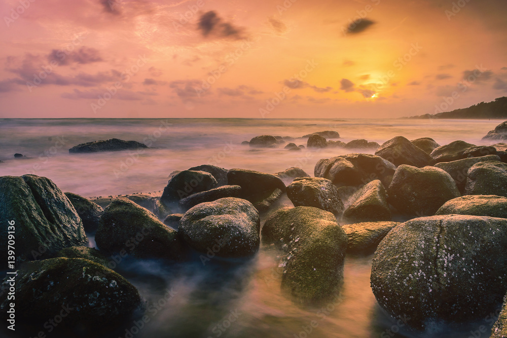 Sunset on the coast of the Thailand at dawn with rocks in foreground.