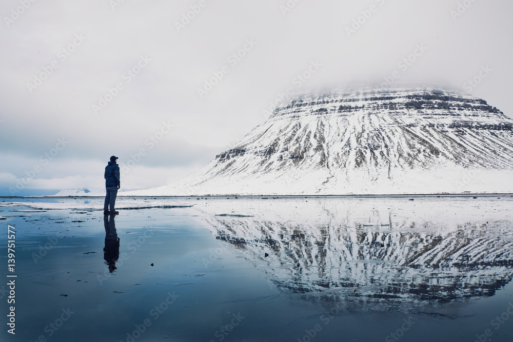 Man standing on an icy lake in front of a mountain engulfed in clouds 