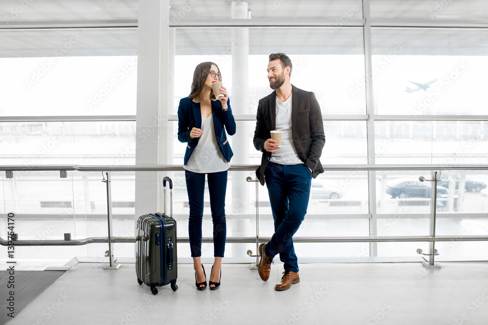 Business couple standing together with baggage and coffee cups near the window at the departure area