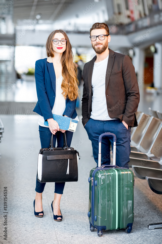 Elegant business couple standing with suitcase and airplane tickets at the waiting hall in the airpo