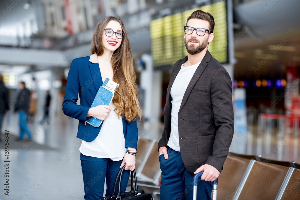 Elegant business couple standing with suitcase and airplane tickets at the waiting hall in the airpo