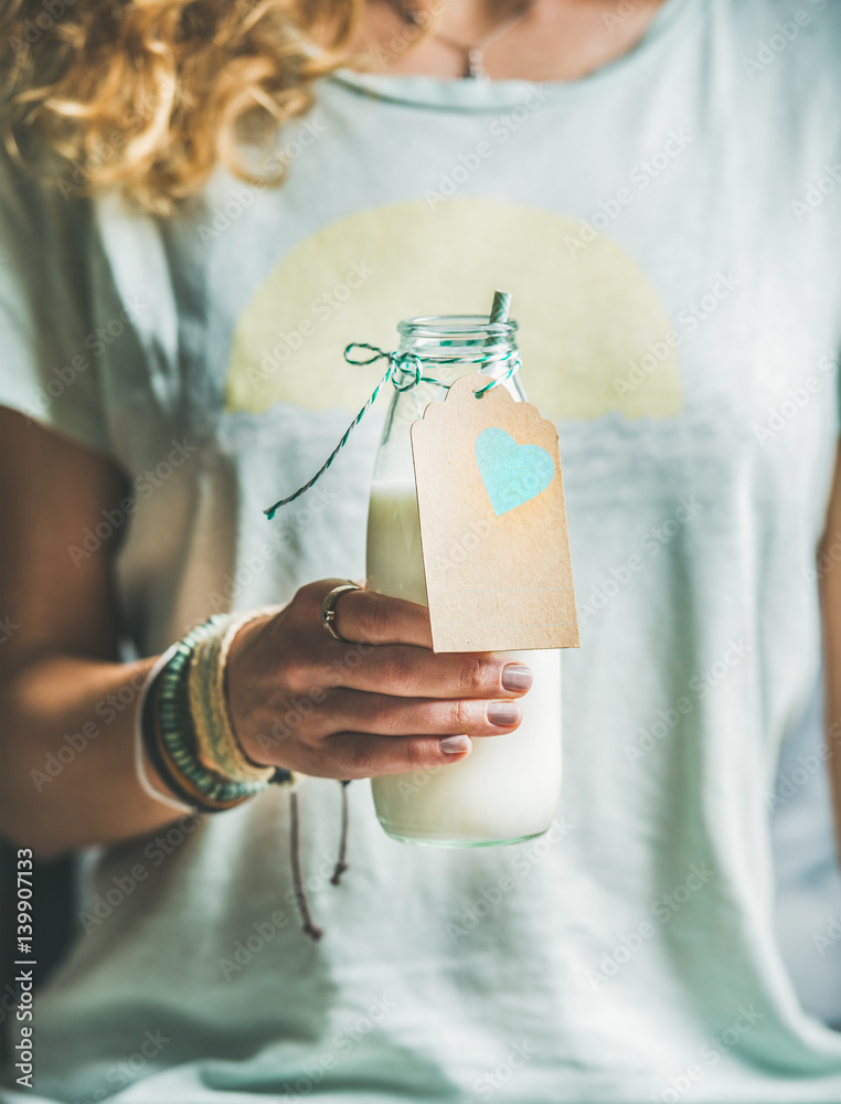 Young blond woman in light t-shirt holding bottle of dairy-free almond milk in her hand. Clean eatin