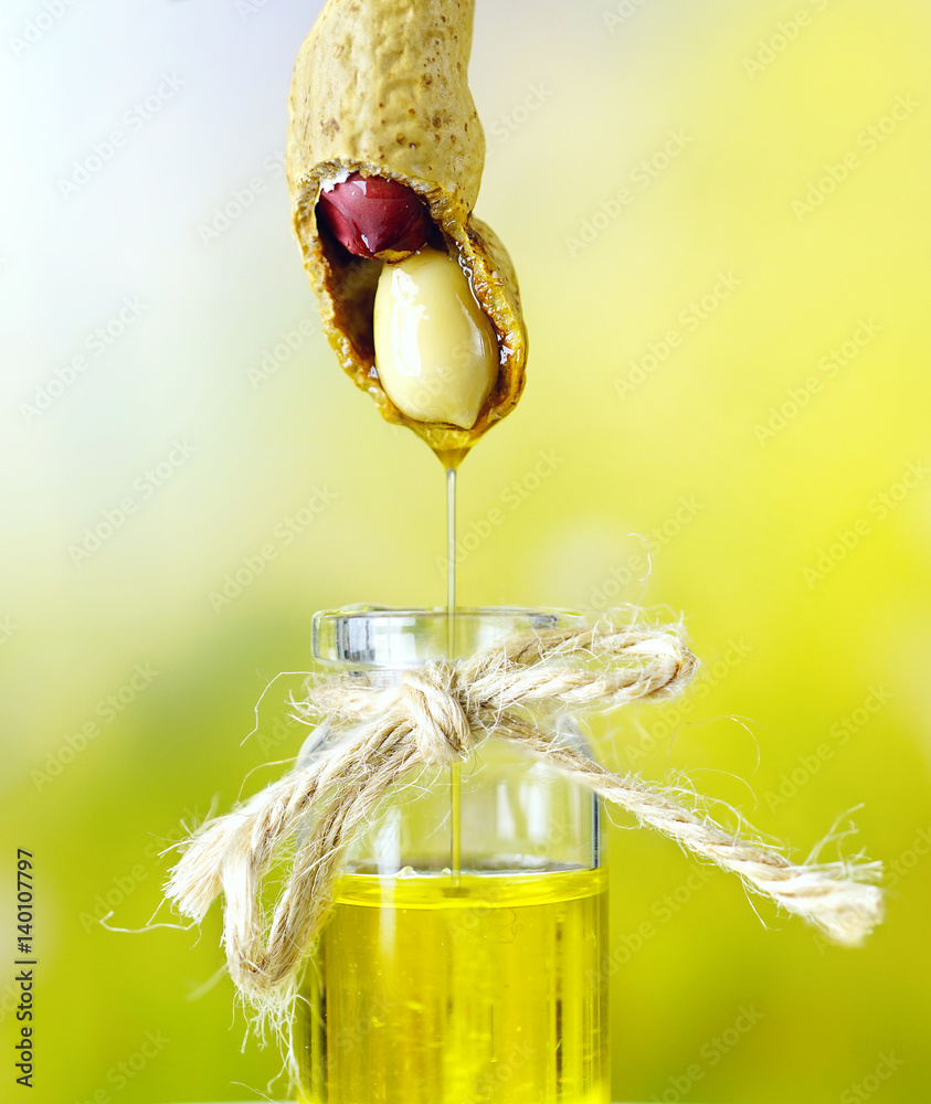 Golden oil peanut drains fall drops from a nut into bottle a close-up macro on a yellow and green ba