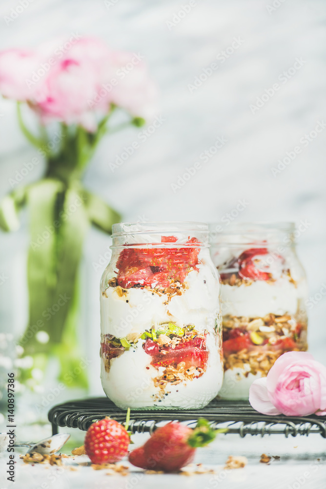 Healthy spring breakfast. Greek yogurt, granola, strawberry breakfast jars, pink raninkulus flowers,