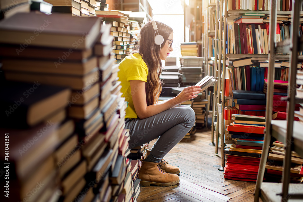 年轻的女学生坐在旧图书馆的一堆书上听音乐