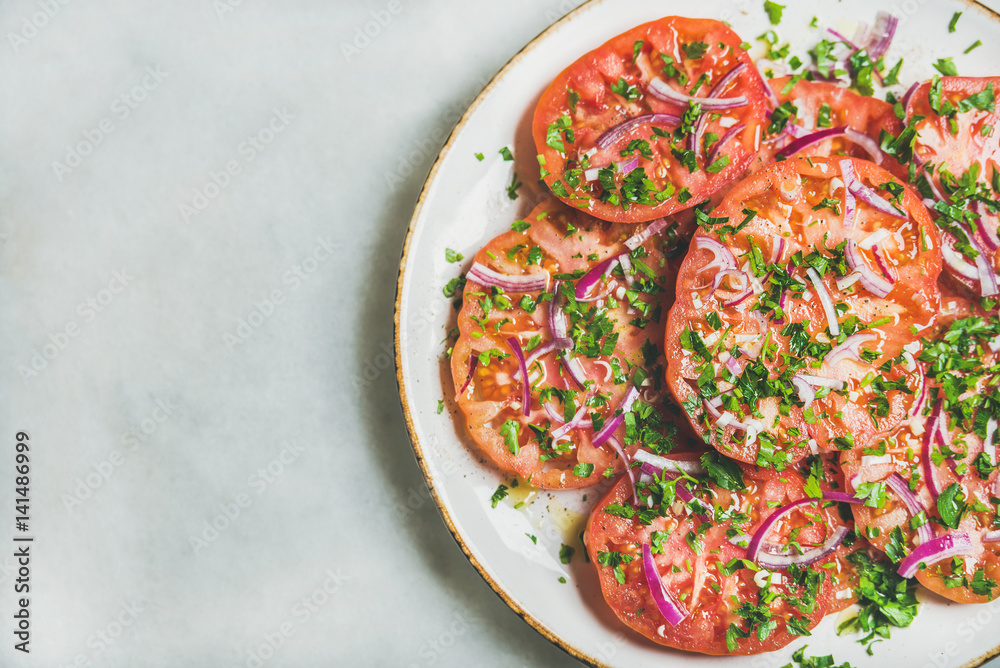Fresh heirloom tomato, parsley and onion salad in white plate over light grey marble background, top