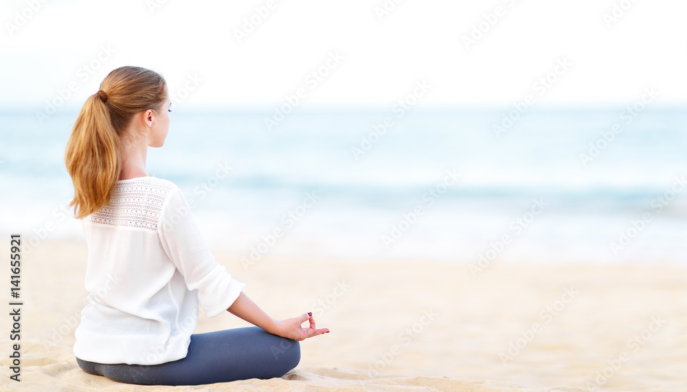 woman practices yoga and meditates in lotus position on beach