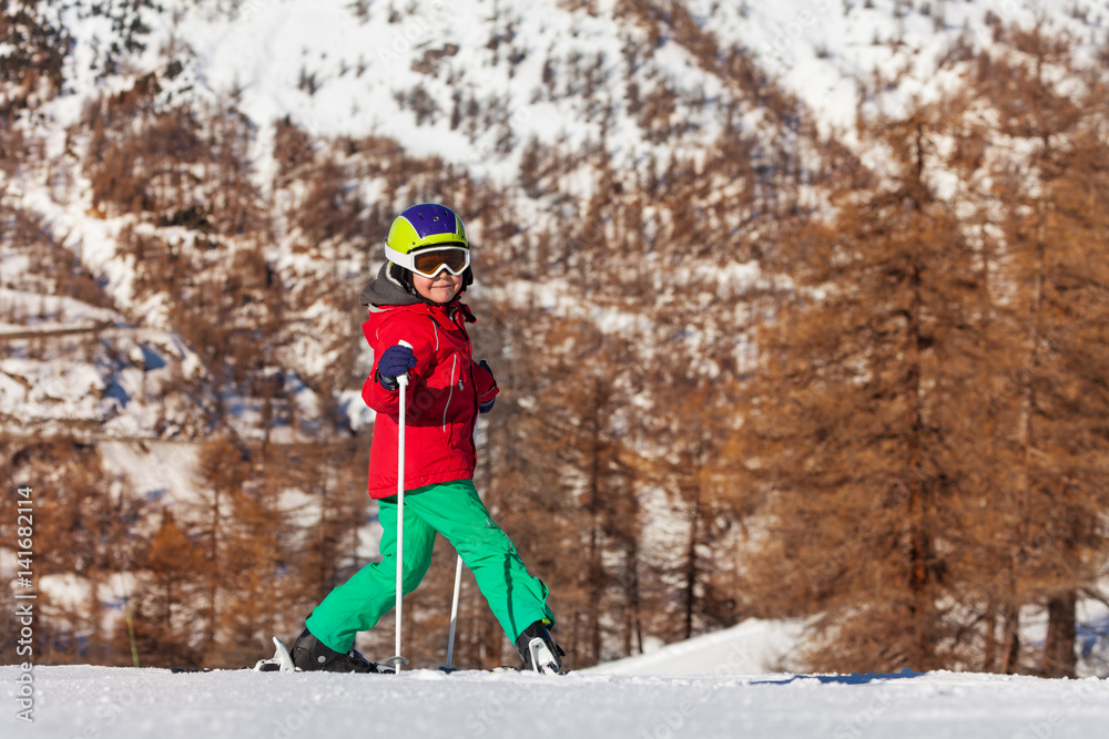 Happy kid boy going on ski at snowy mountains
