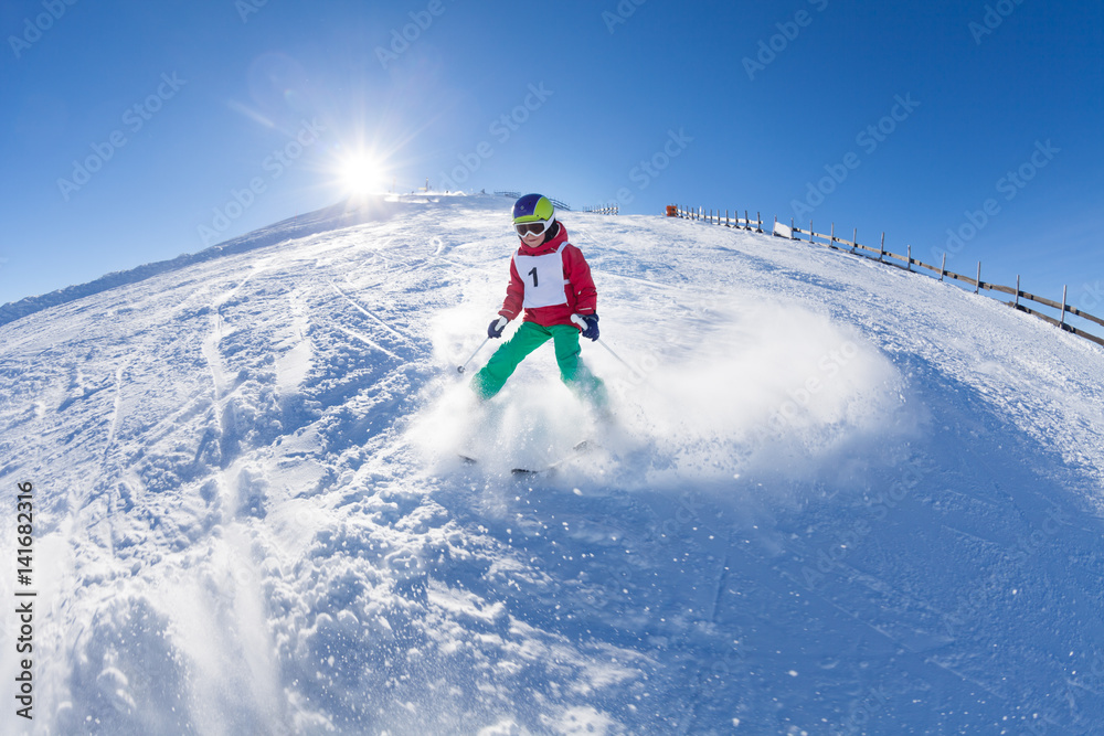Little skier walking down the hill in mountains