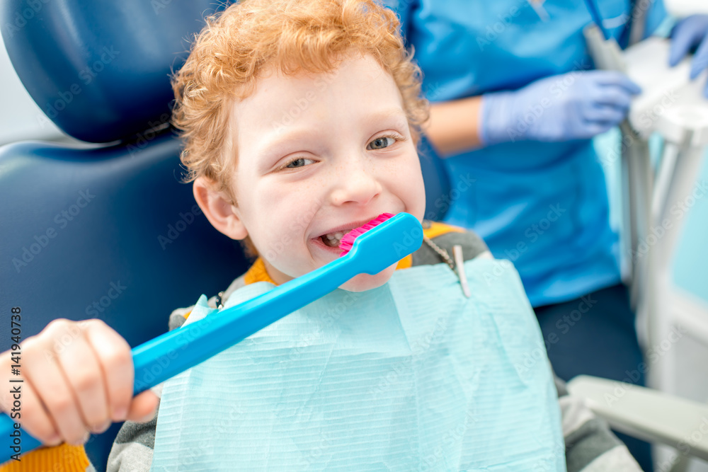 小男孩坐在牙科诊所的椅子上用大牙刷刷牙