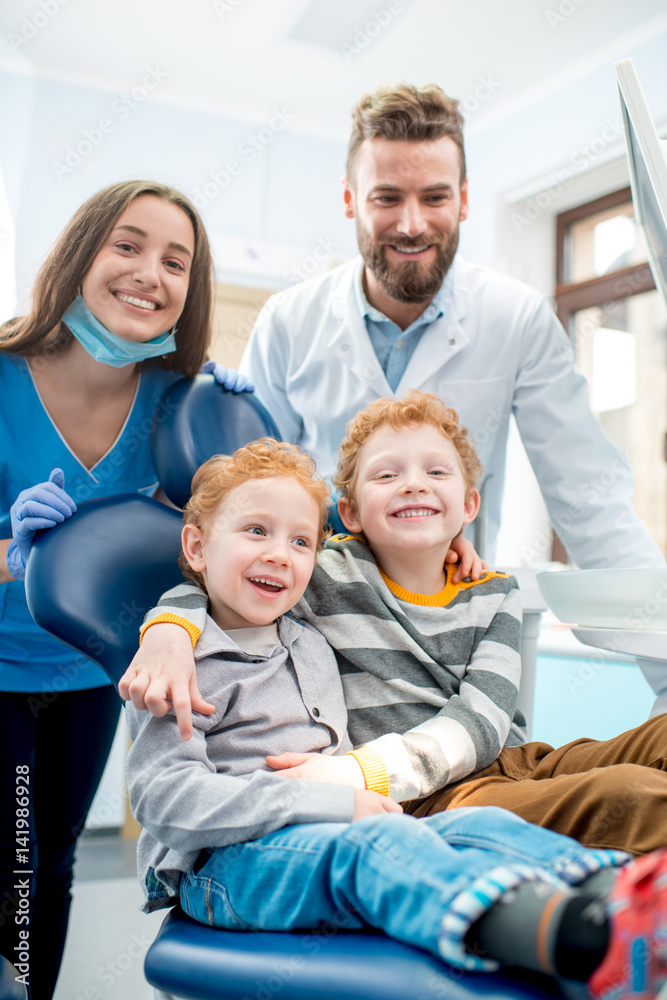 Portrait of happy young boys sitting on the chair with dentist and woman assistant at the dental off