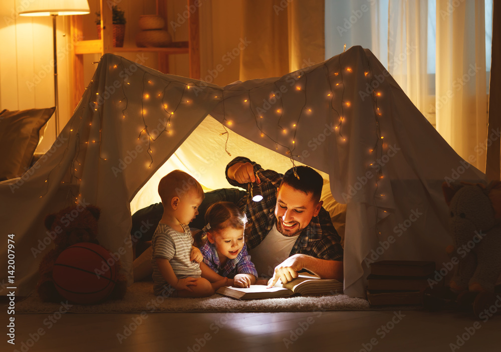 幸福的家庭父亲和孩子们在家里的帐篷里看书。
