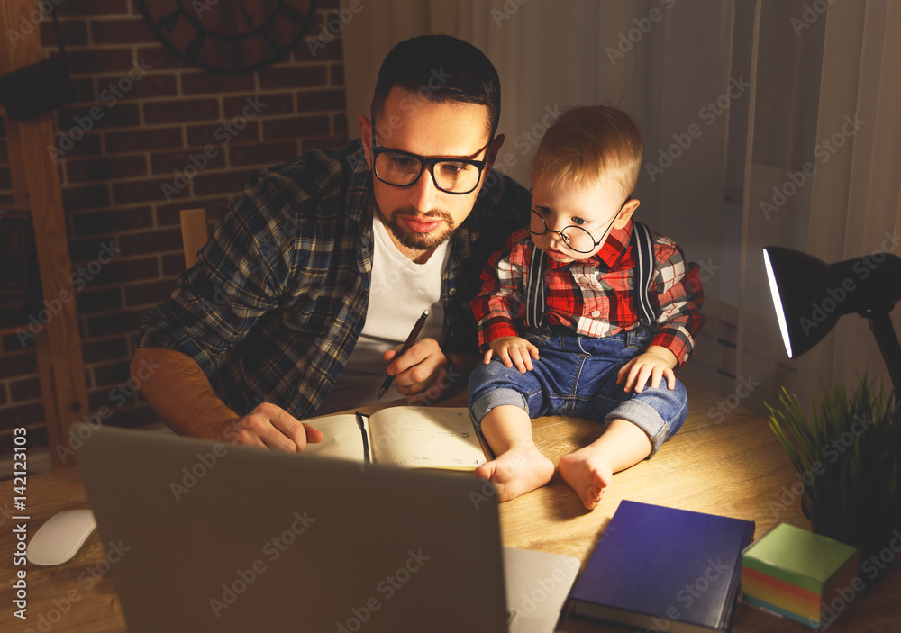 father and son baby work at home at computer in dark .