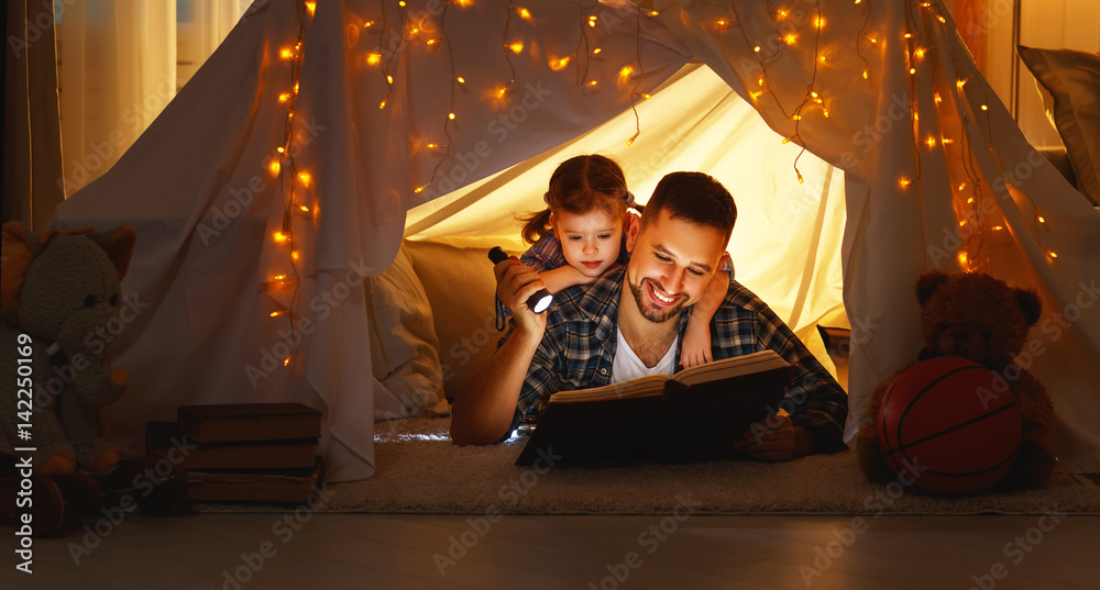幸福的家庭父亲和孩子在家里的帐篷里看书。