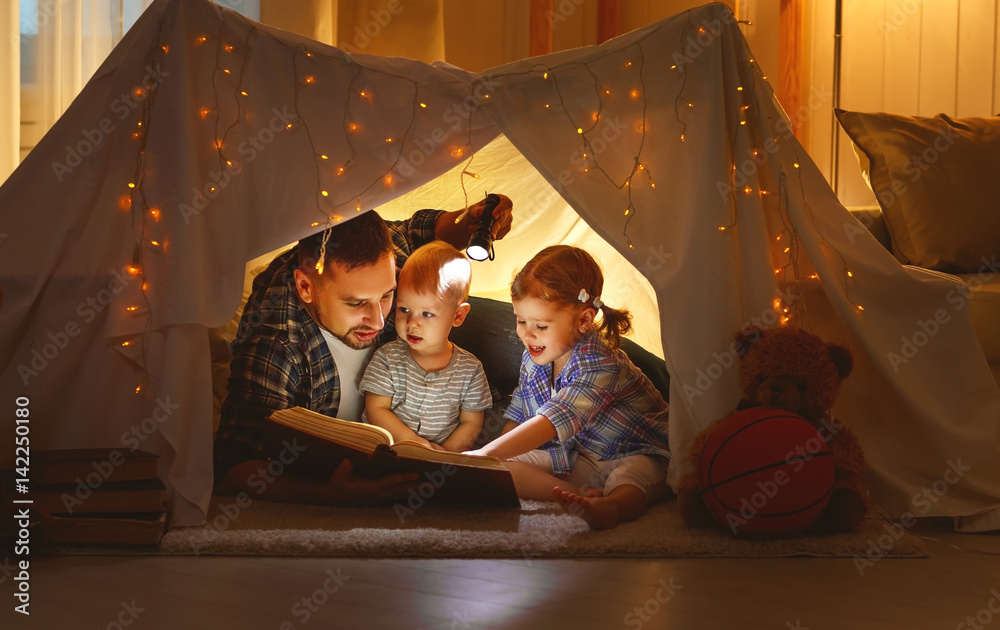 幸福的家庭父亲和孩子们在家里的帐篷里看书。