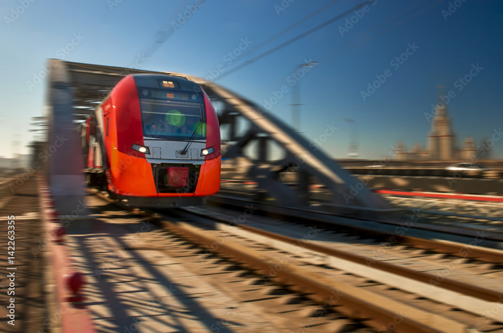 亮红色高速列车在高层建筑的背景下驶出跨江大桥