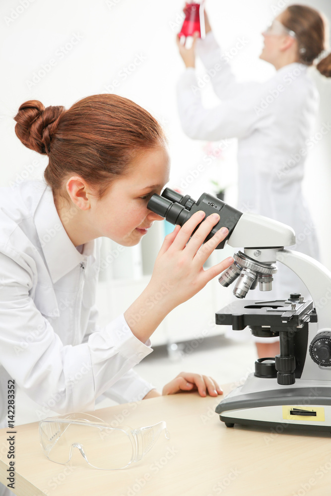漂亮的女学生在化学课上透过显微镜看