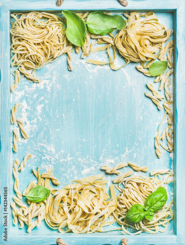 各种自制的新鲜未煮意大利意大利面，用面粉和绿色罗勒叶放在蓝色木托盘里。