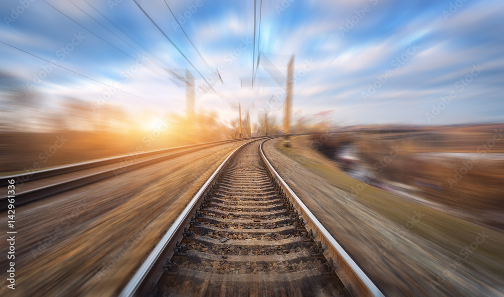 Railroad in motion at sunset. Railway station with motion blur effect and colorful sky with clouds. 