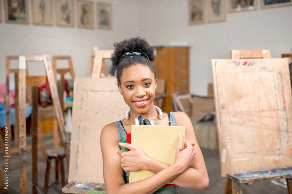 Portrait of a young african ethnicity student holding books at the studio for painting