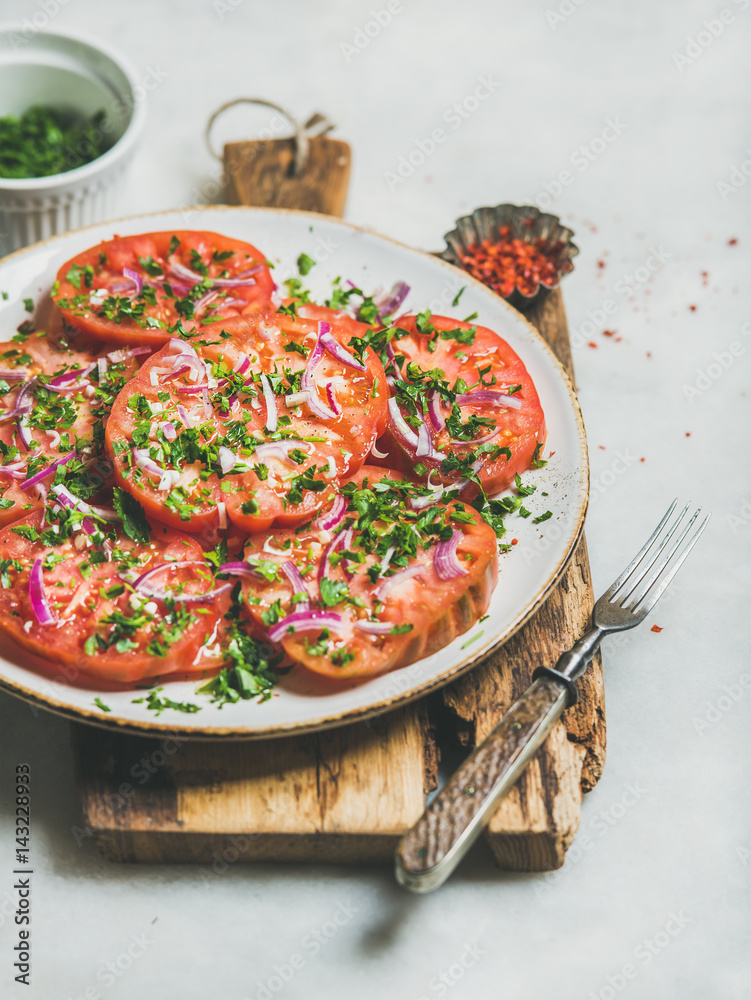 新鲜的传家宝番茄、欧芹和洋葱沙拉，装在浅灰色大理石上的木板上的白色盘子里