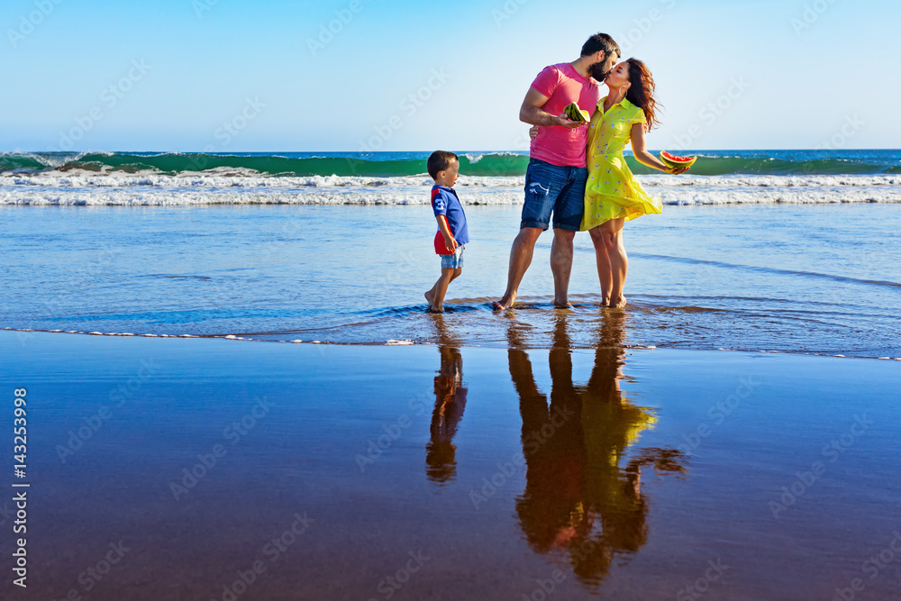 幸福的家庭——父亲、母亲、小儿子在黑色沙滩上的游泳池旁散步，海浪拍打。人们