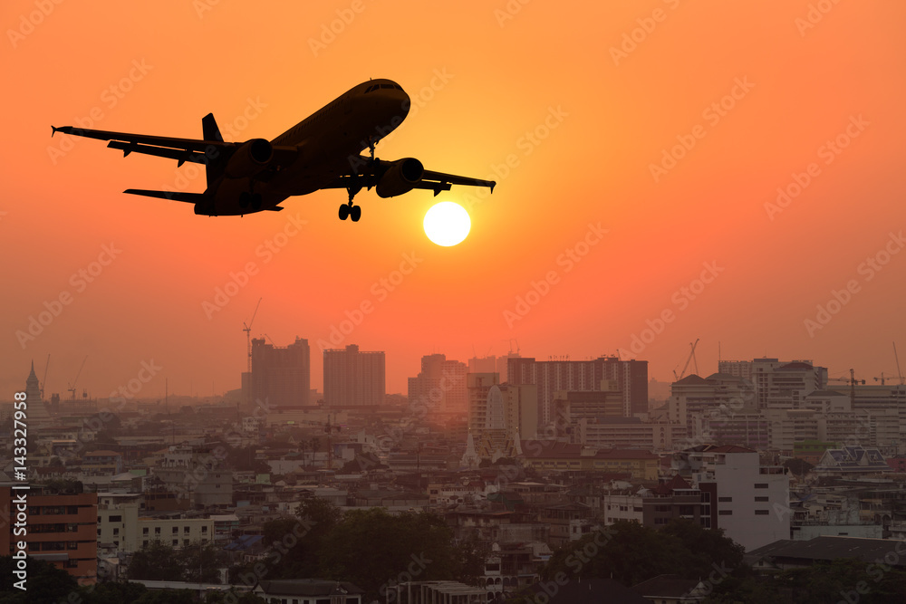 日落时在城市上空飞行的剪影商用飞机