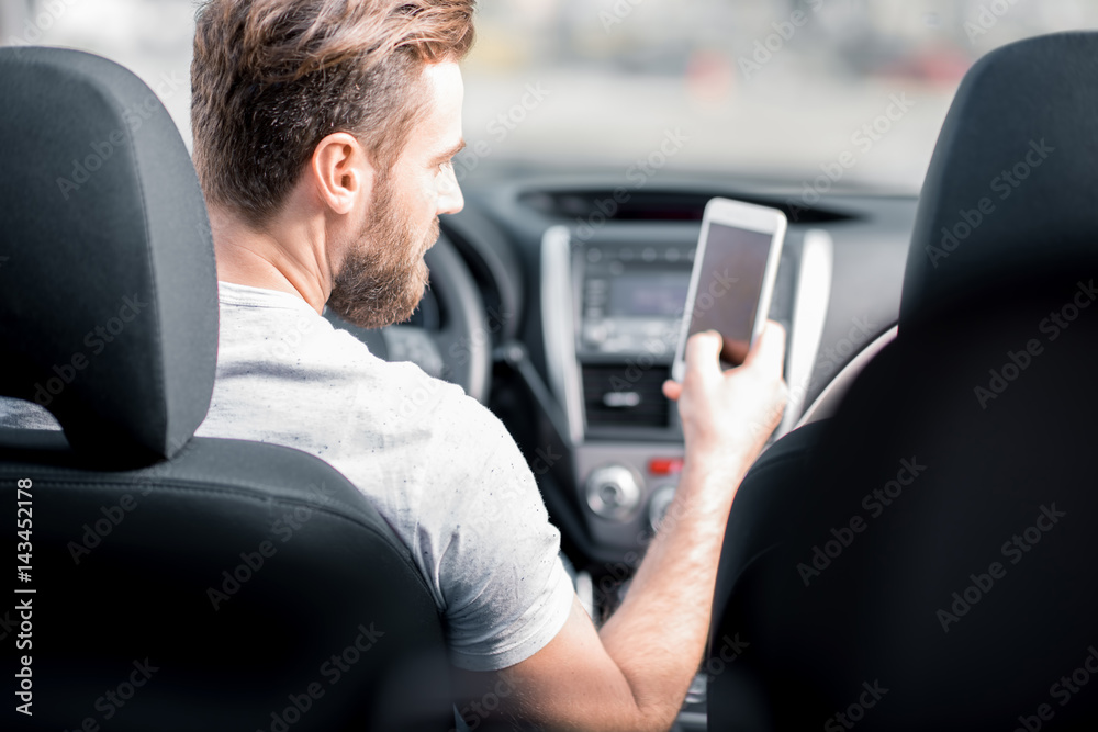 一名男子坐在汽车前排座位上使用智能手机。后视图聚焦于面部
