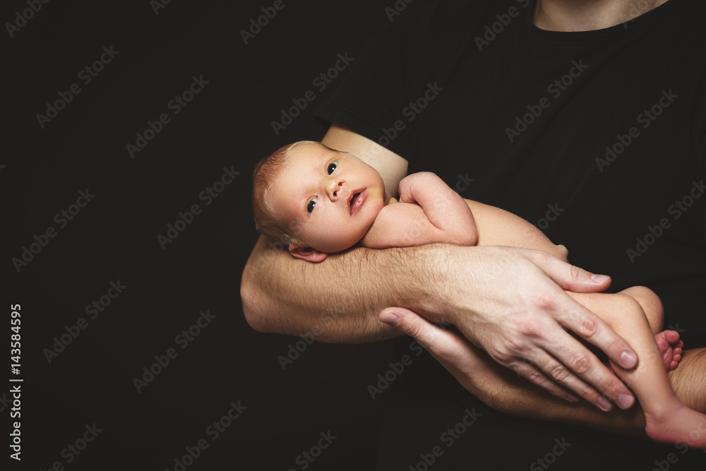 Newborn baby in his fathers hands in dark