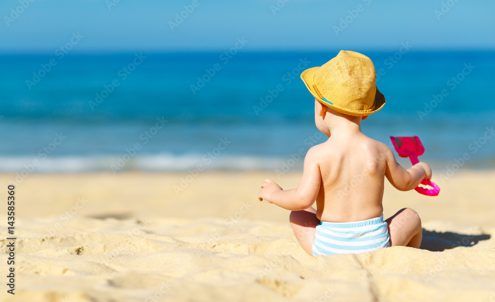 男婴在海滩上拿着玩具坐着