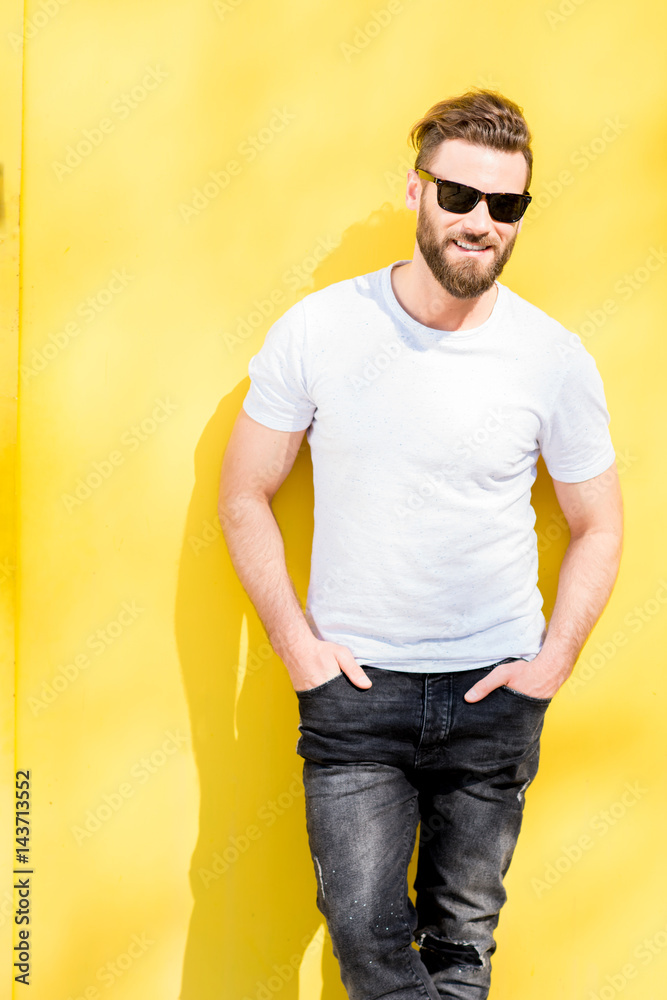 黄色背景下，一位身穿白色t恤和牛仔裤的英俊男子的彩色肖像