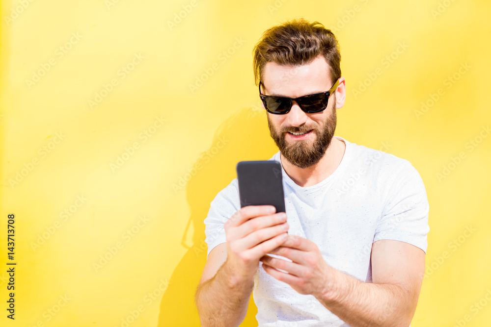 一个穿着白色t恤的英俊男子在黄色背景上使用手机的彩色肖像