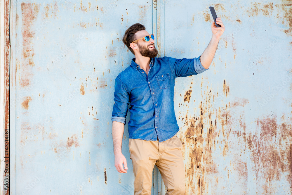 穿着蓝色t恤的英俊男子，锈迹斑斑的旧墙背景上有手机