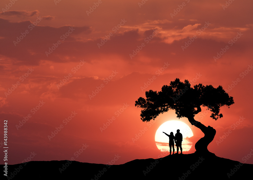 太阳背景下弯曲的树下的人。一对站在山上的夫妇的剪影
