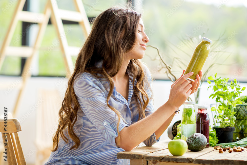 美丽的女人坐在家里，喝着饮料和健康的绿色食品。素食和排毒概念