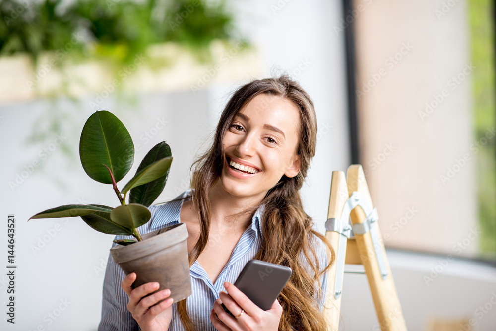 年轻女子站在梯子上，拿着电话和花盆，用绿色植物种植家园
