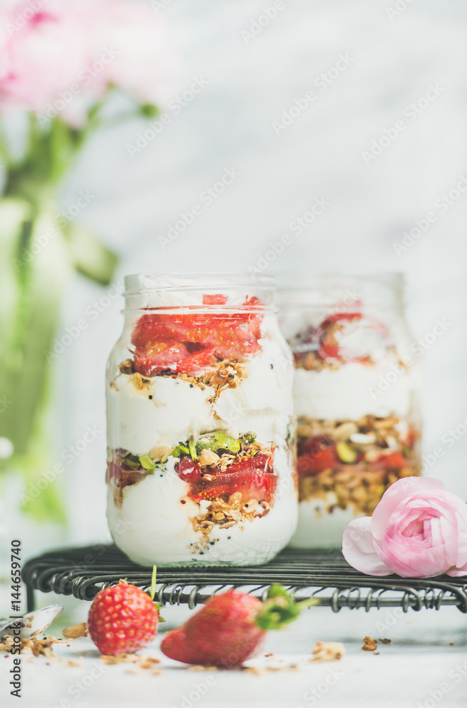 健康的春季早餐。希腊酸奶、格兰诺拉麦片、新鲜草莓早餐罐、粉色raninkulus fl