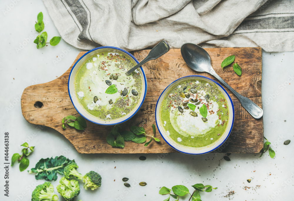 Spring detox broccoli green cream soup with mint and coconut cream in bowls on rustic wooden board o
