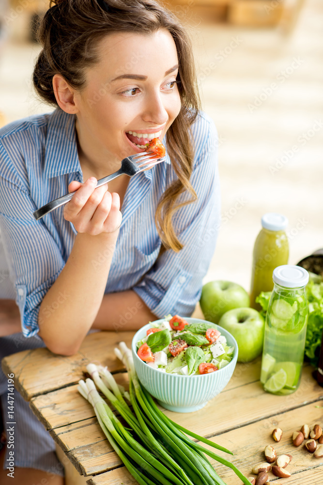 年轻快乐的女人在室内用绿色新鲜食材坐在桌子上吃健康沙拉