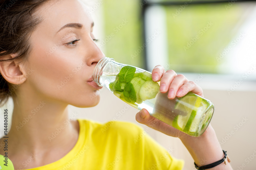 一名女子在用哑铃锻炼时喝薄荷、黄瓜和酸橙水的特写。Det