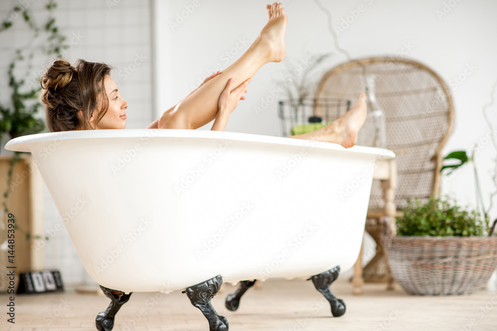漂亮的年轻女人躺在浴室的浴缸里照顾腿