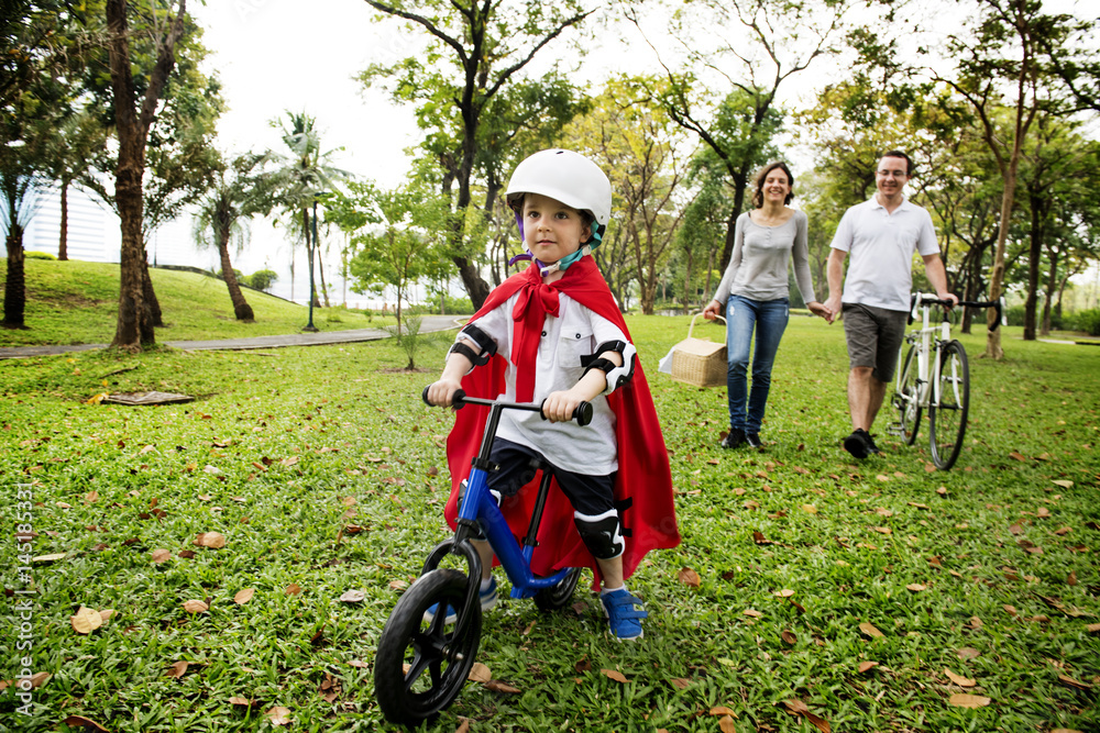 超级英雄小男孩与家人在公园里骑自行车