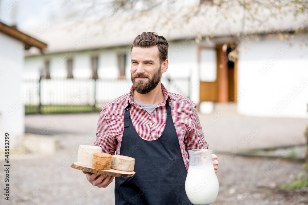 Portrait of a handsome farmer in apron walking with goat cheeses and milk outdoors on the rural hous